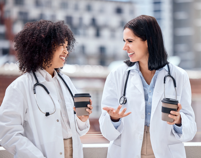 Two female physicians talking with coffee cups in hand