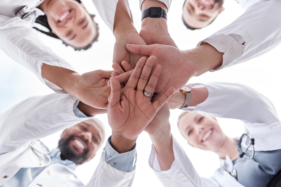 Four healthcare workers in a circle with their hands in the center